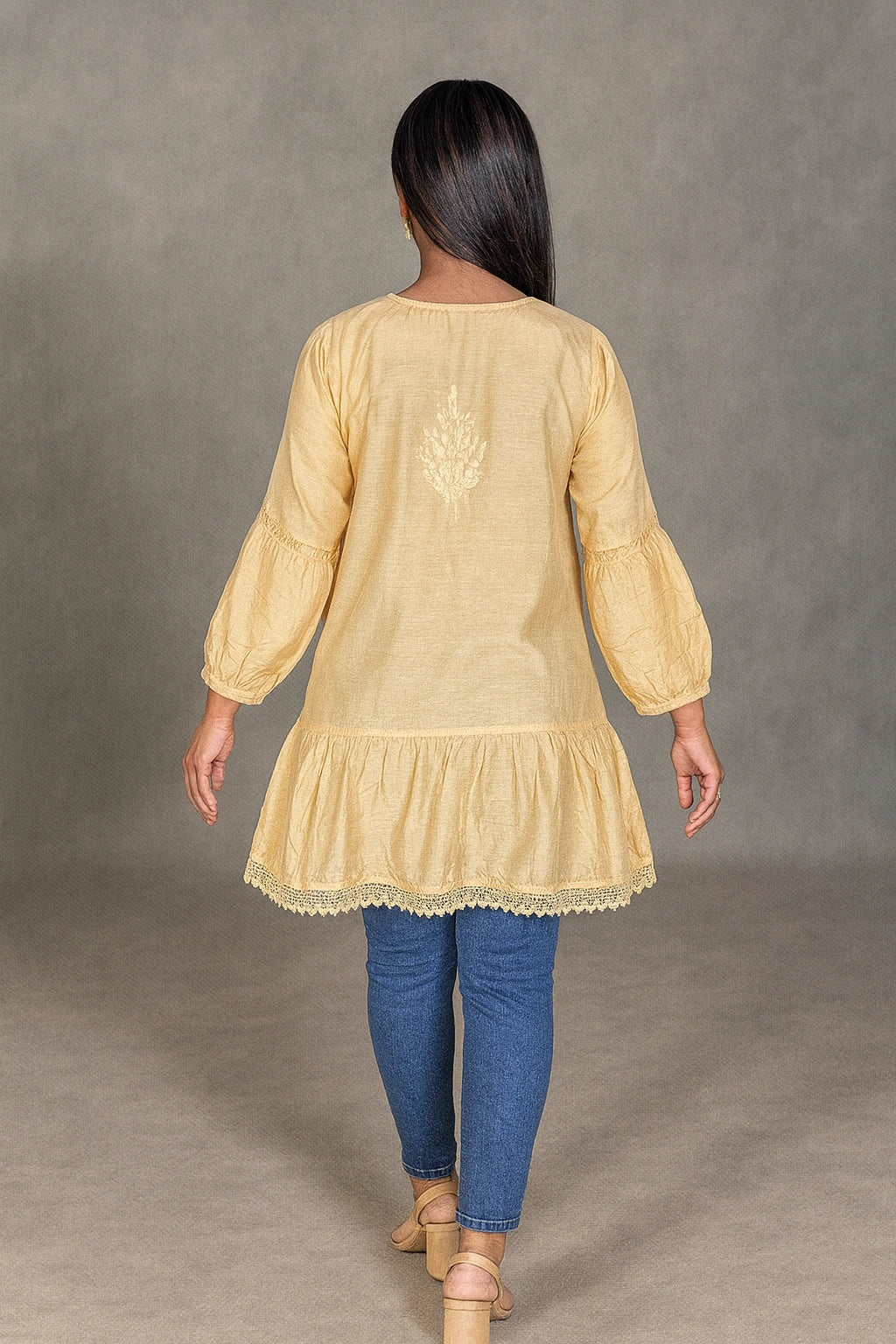 Woman wearing a lucknowi chikankari yellow kurta with blue pants against a gray background