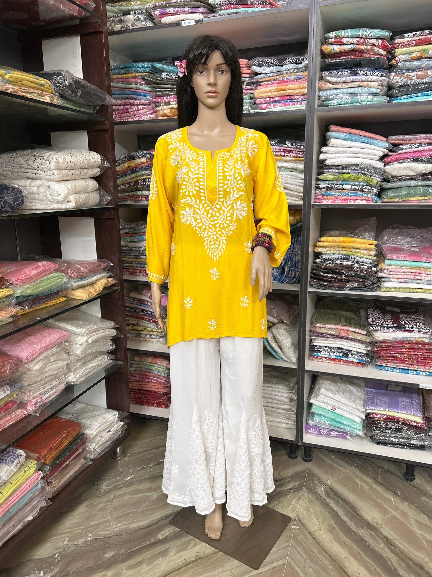 Mannequin wearing a yellow embroidered top and white pants in a fabric store.