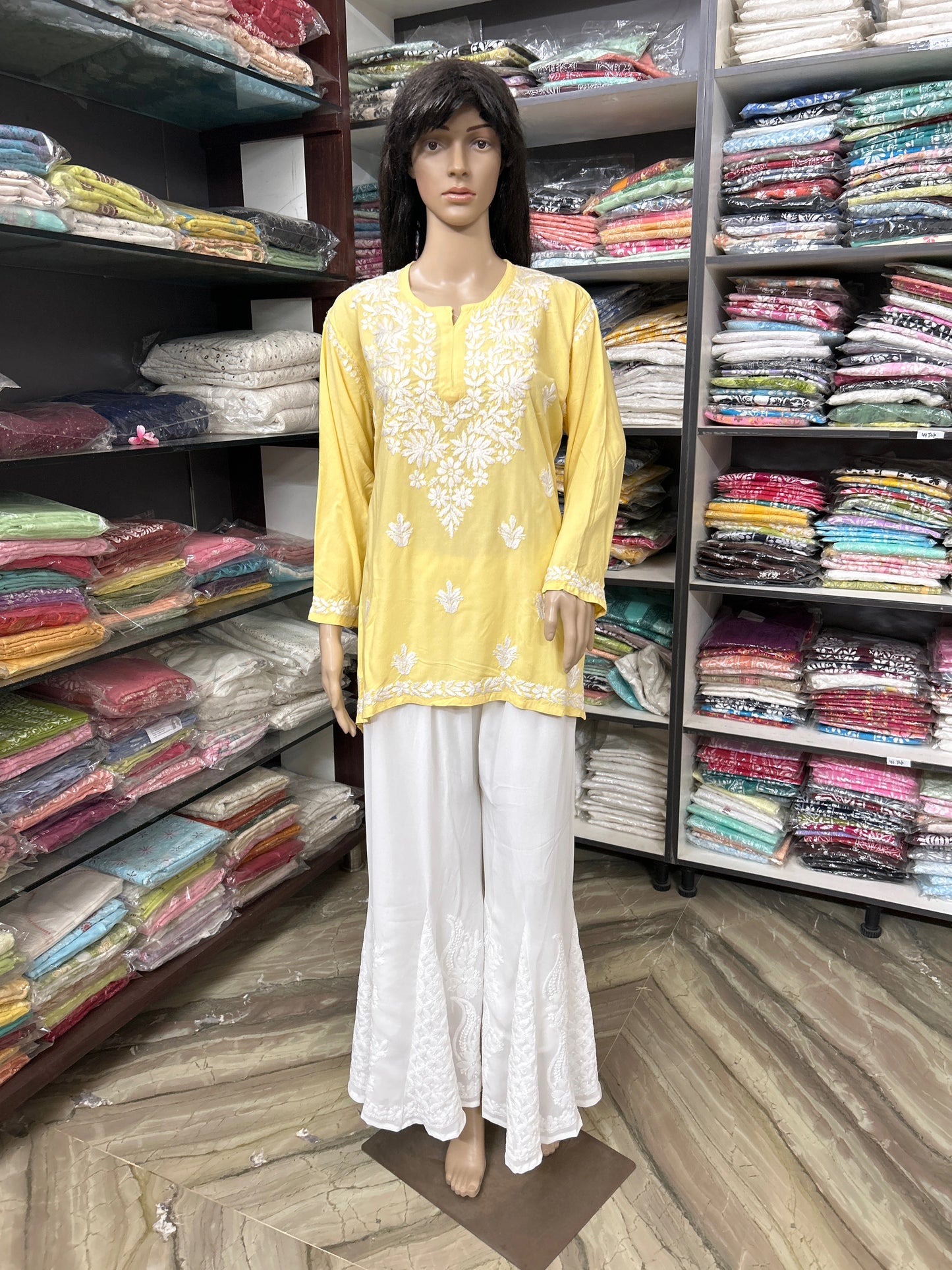 Mannequin wearing a yellow embroidered top and white pants in a fabric store.
