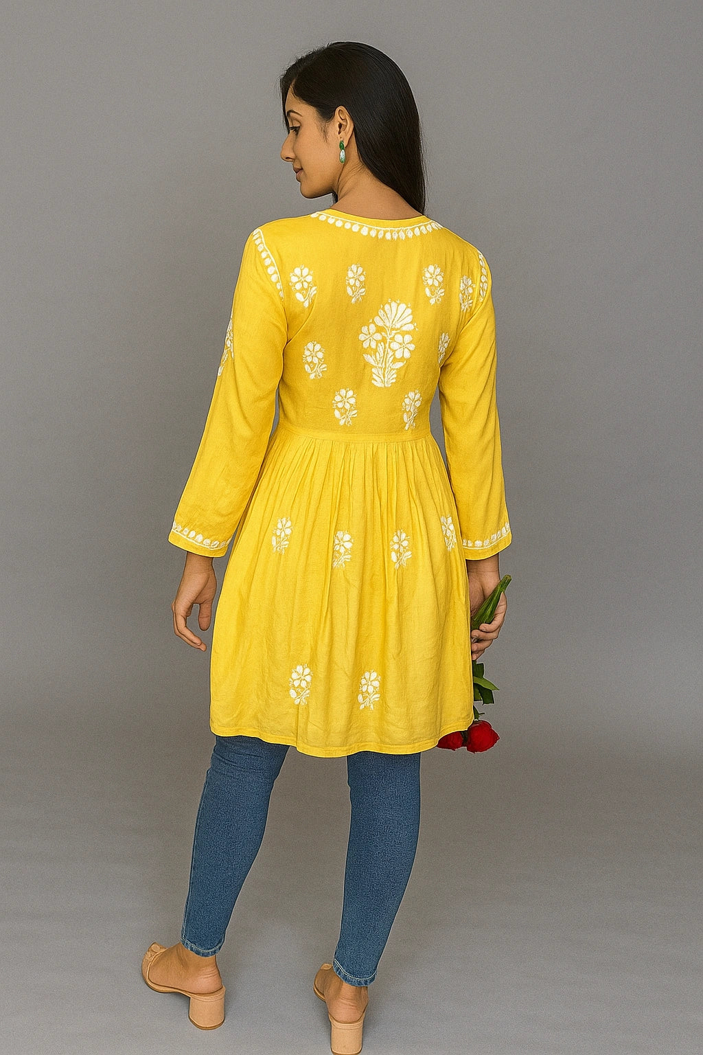Woman wearing a yellow embroidered dress with blue pants against a gray background