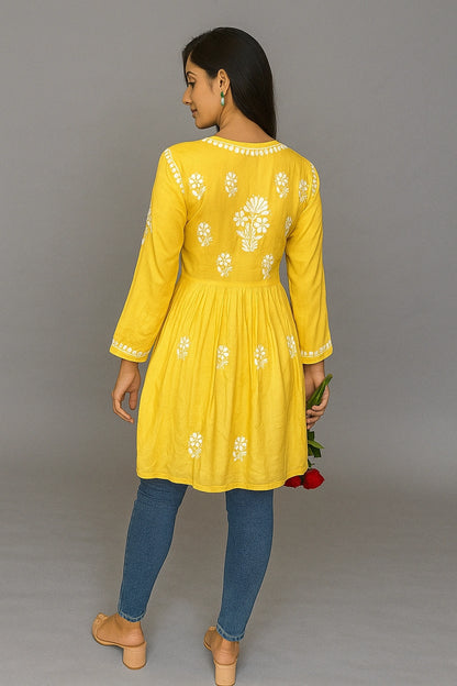 Woman wearing a yellow embroidered dress with blue pants against a gray background