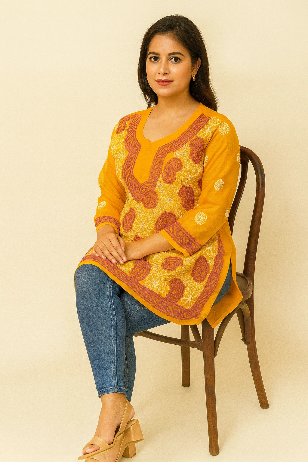 Woman wearing a lucknowi chikankari yellow patterned top sitting on a chair against a beige background