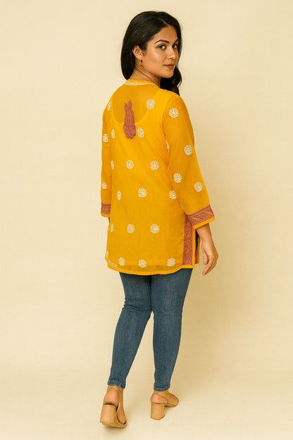 Woman wearing a lucknowi chikankari yellow top with white patterns and blue jeans on a beige background