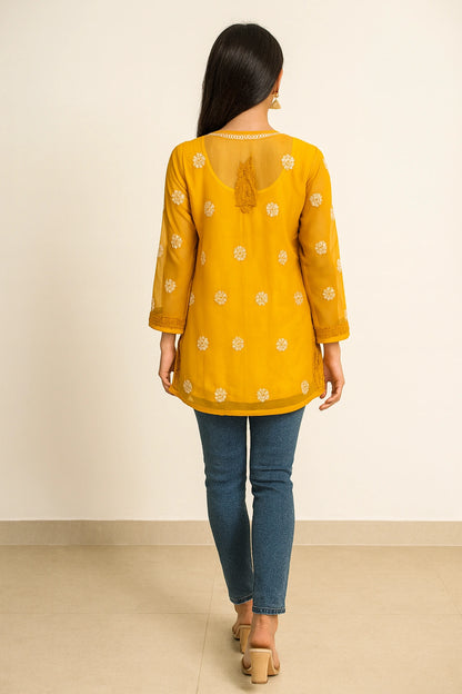 Woman wearing a lucknowi chikankari yellow top with floral patterns and blue jeans on a beige background