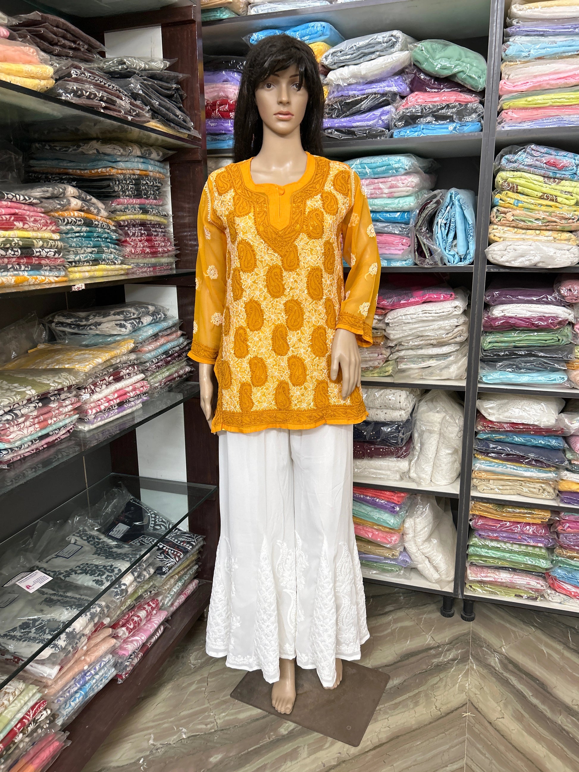 Mannequin wearing a lucknowi chikankari yellow patterned top and white pants in a fabric store.