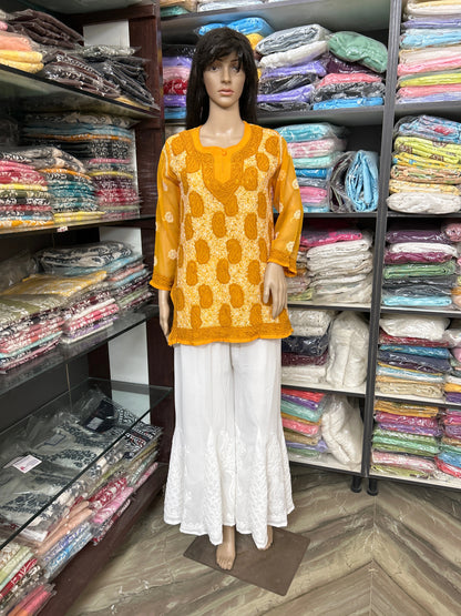 Mannequin wearing a lucknowi chikankari yellow patterned top and white pants in a fabric store.