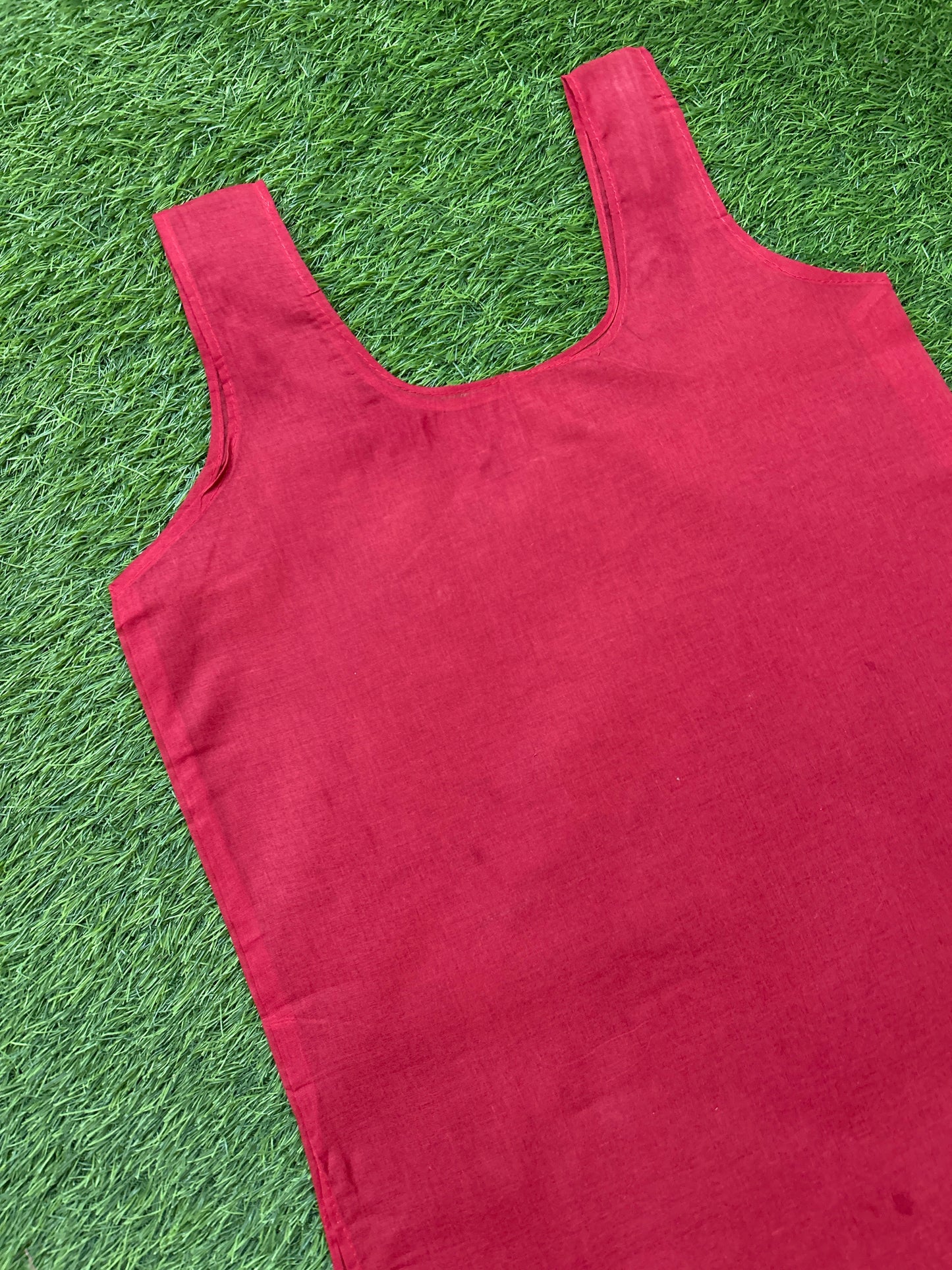 A sleeveless red tank top laid flat on green artificial grass.