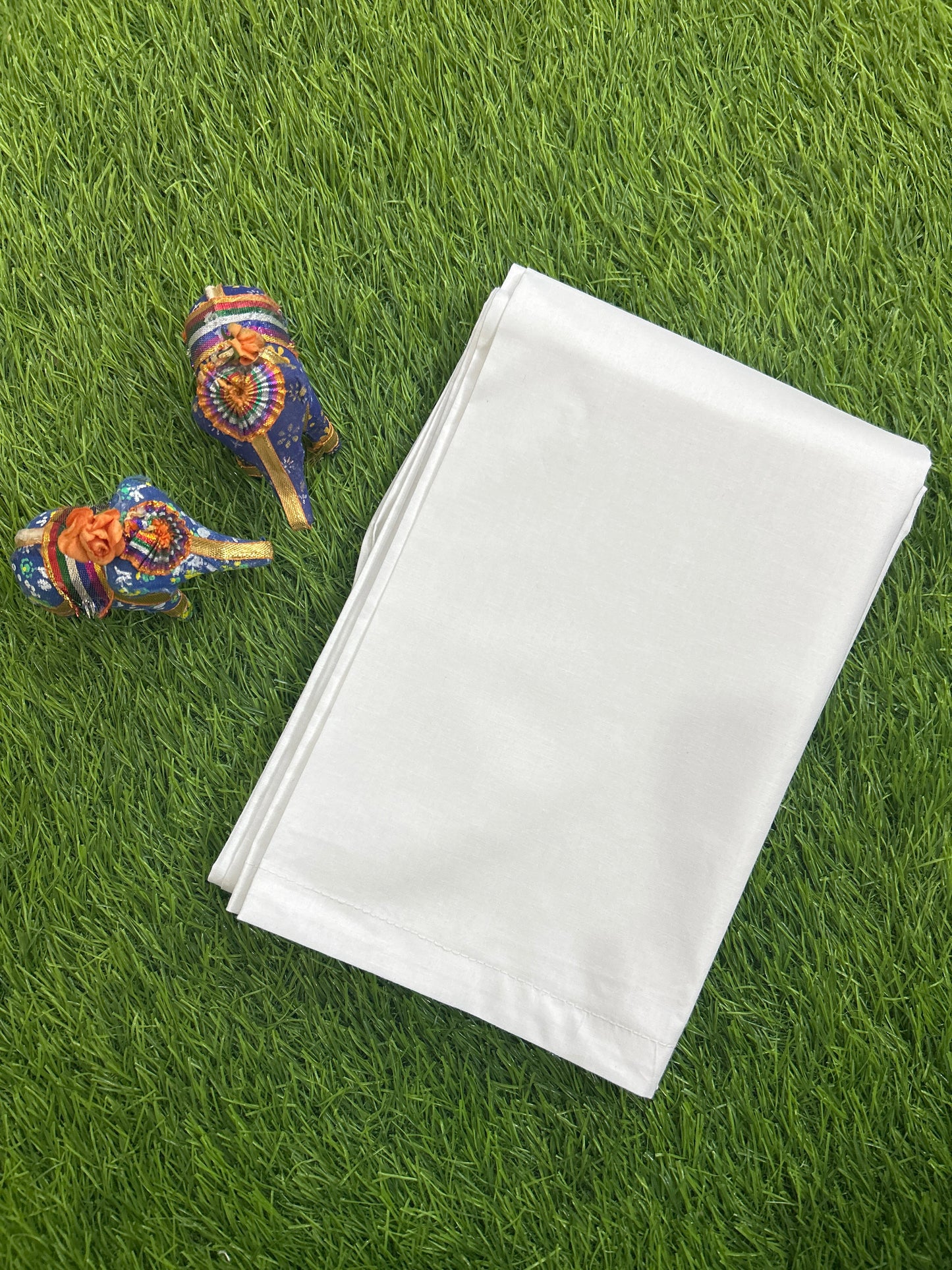 A folded white men's cotton pajama placed on bright green grass, with two small decorative elephant figurines nearby.