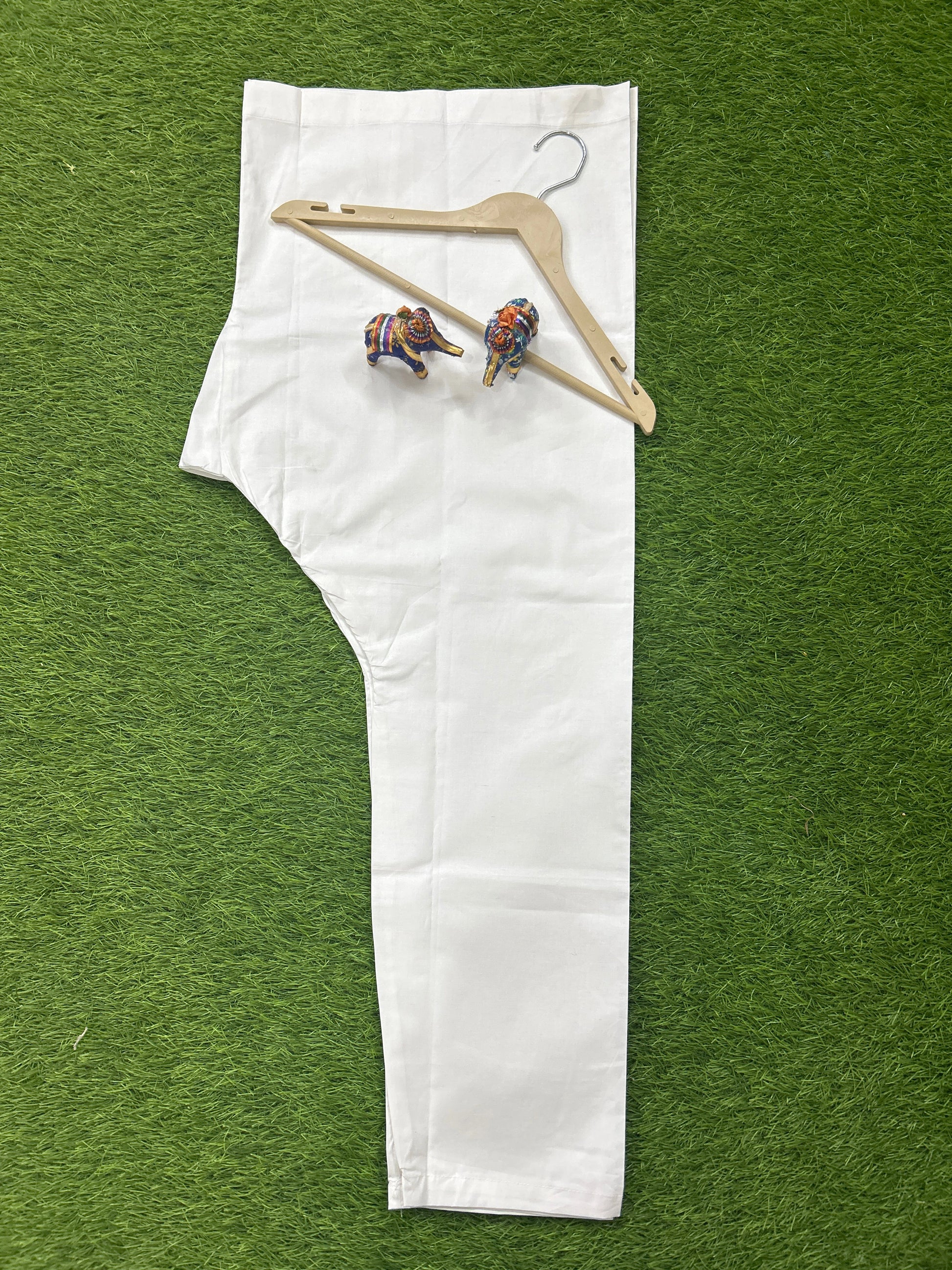 A single white garment laid flat on a green artificial grass background, with a wooden hanger and two small colorful elephant figurines placed on top.